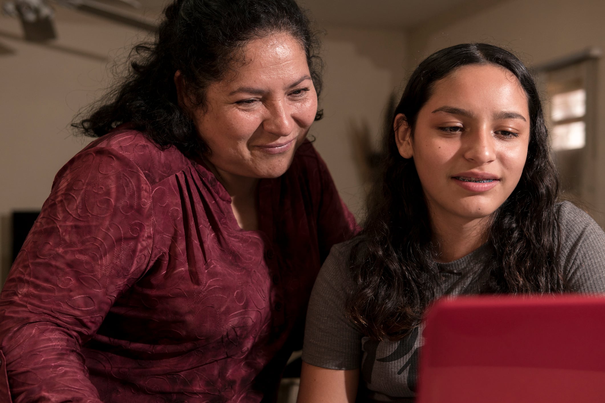A teenager showing her mom something on a red laptop