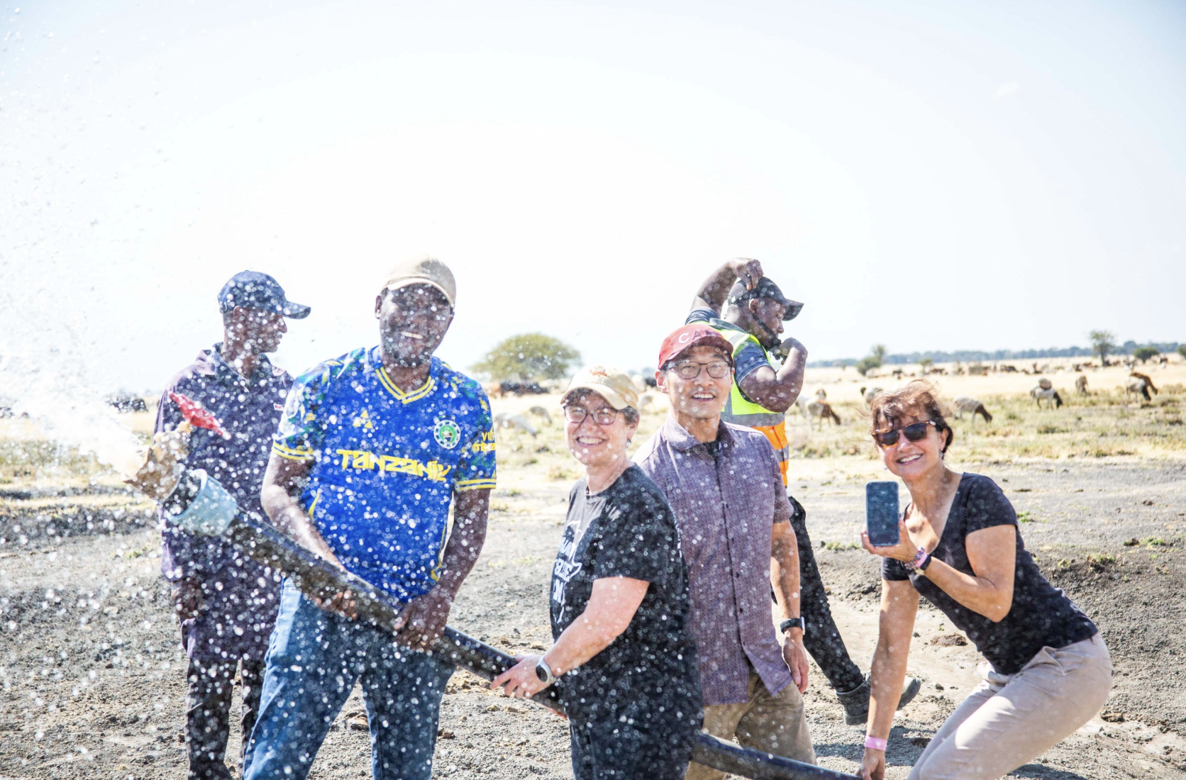 The Bold Challenges Team holds a hose of pipeline and smiles for the camera amidst a spray of water